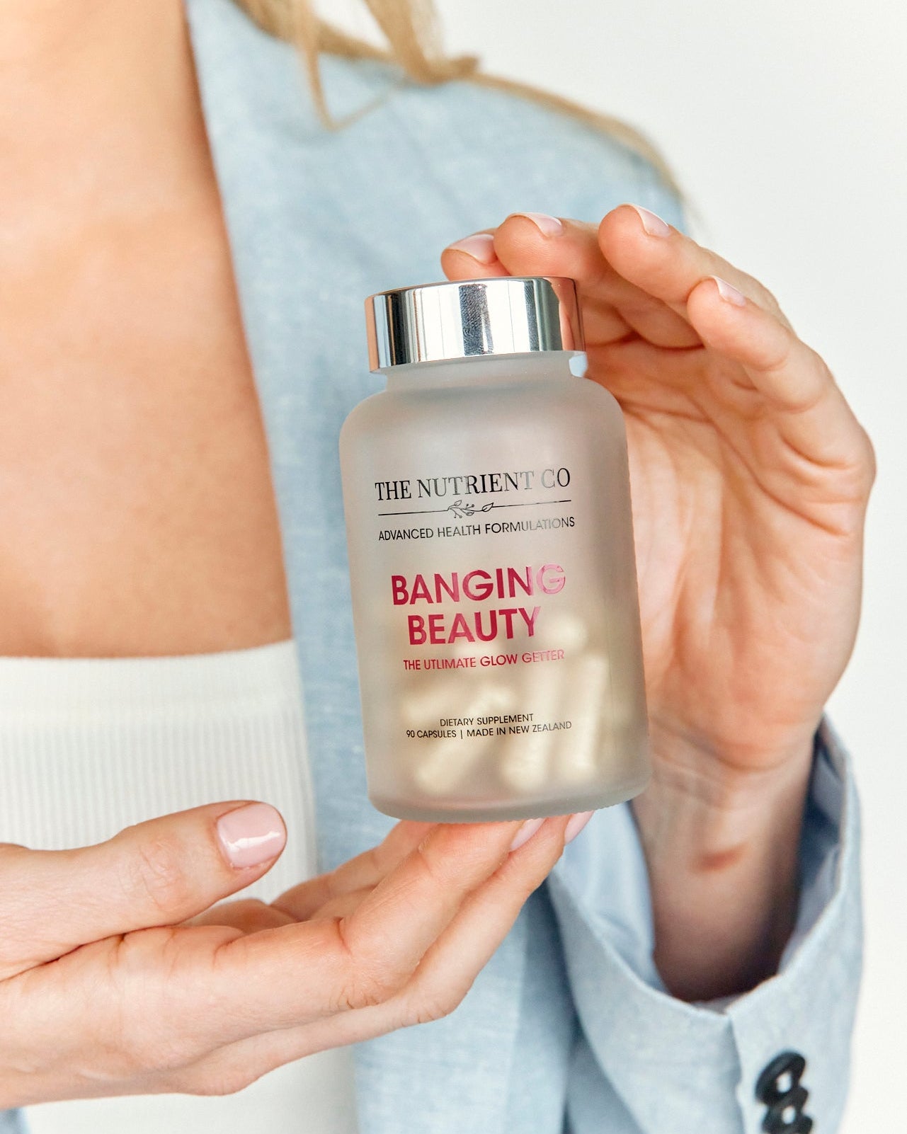 Person holding a supplement container labeled 'Banging Beauty' by The Nutrient Co.