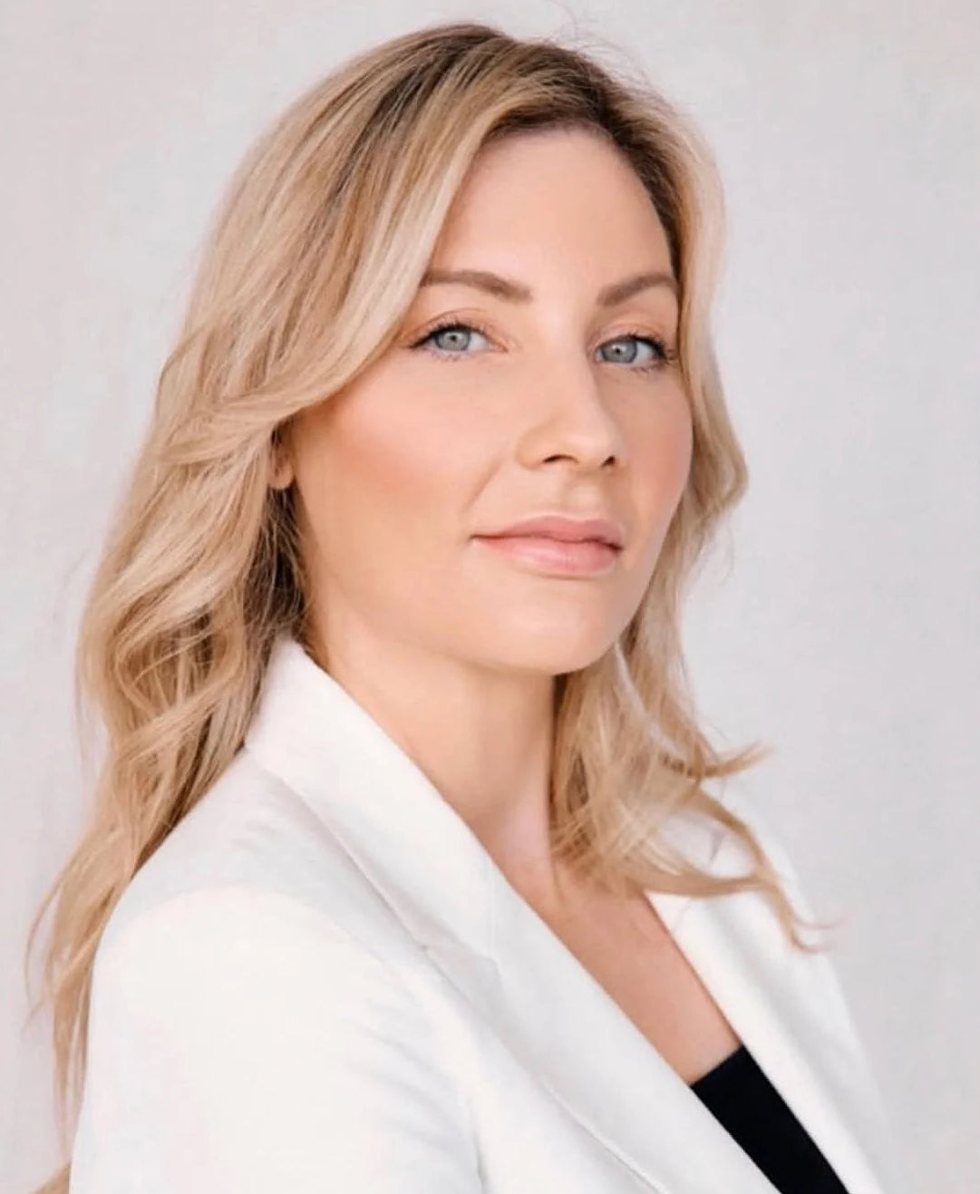 Woman with blonde hair wearing a white blazer against a light background