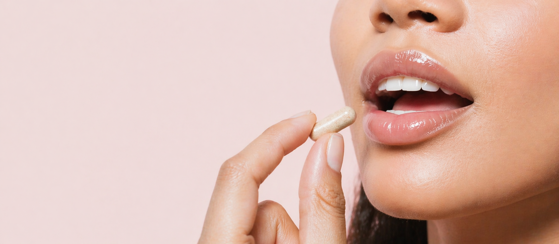 Person holding a vitamin supplement close to their mouth against a pink background