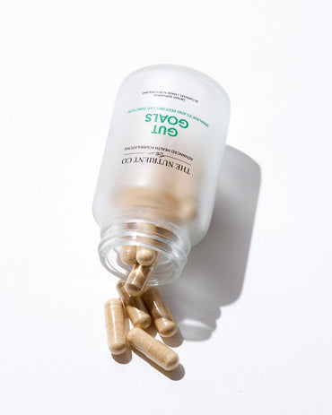 Supplement capsules spilling out of a Gouls container on a white background