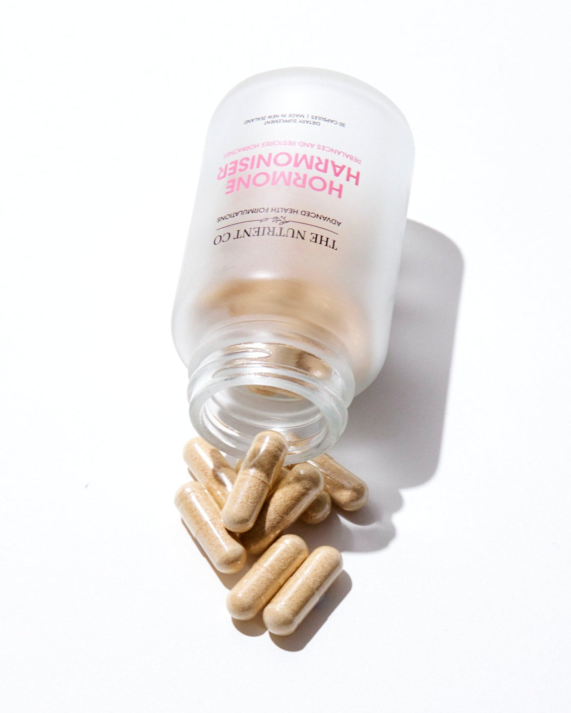 Bottle of Hormone Harmonizing Supplements with pills spilling out on a white background