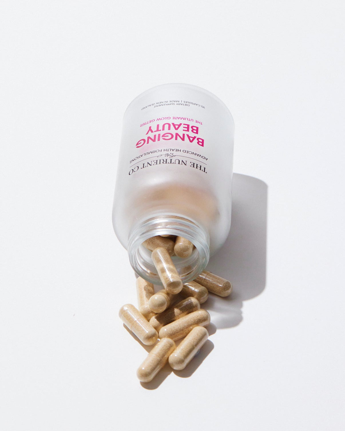 Vitamins or supplements spilling out of a container labeled 'BANGING BEAUTY' on a white background.