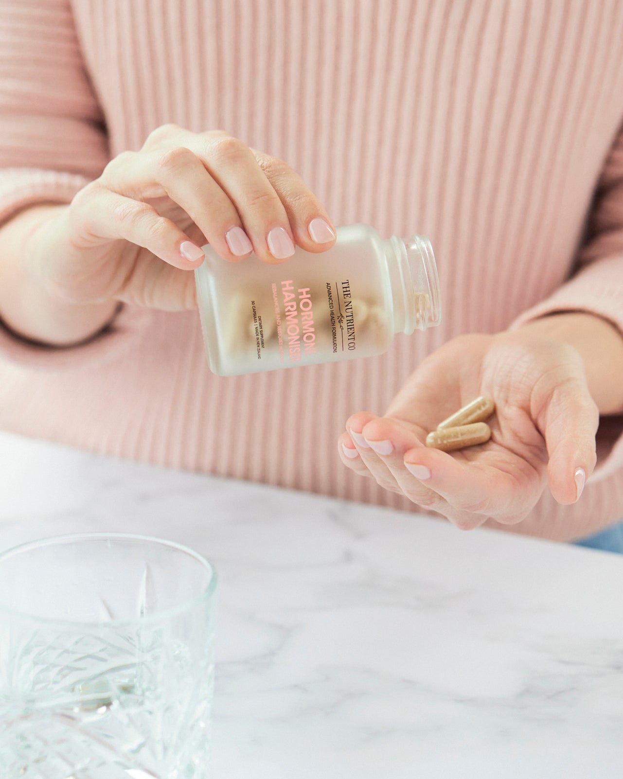 Person holding a bottle of supplements with pills in their hand, wearing a pink sweater.
