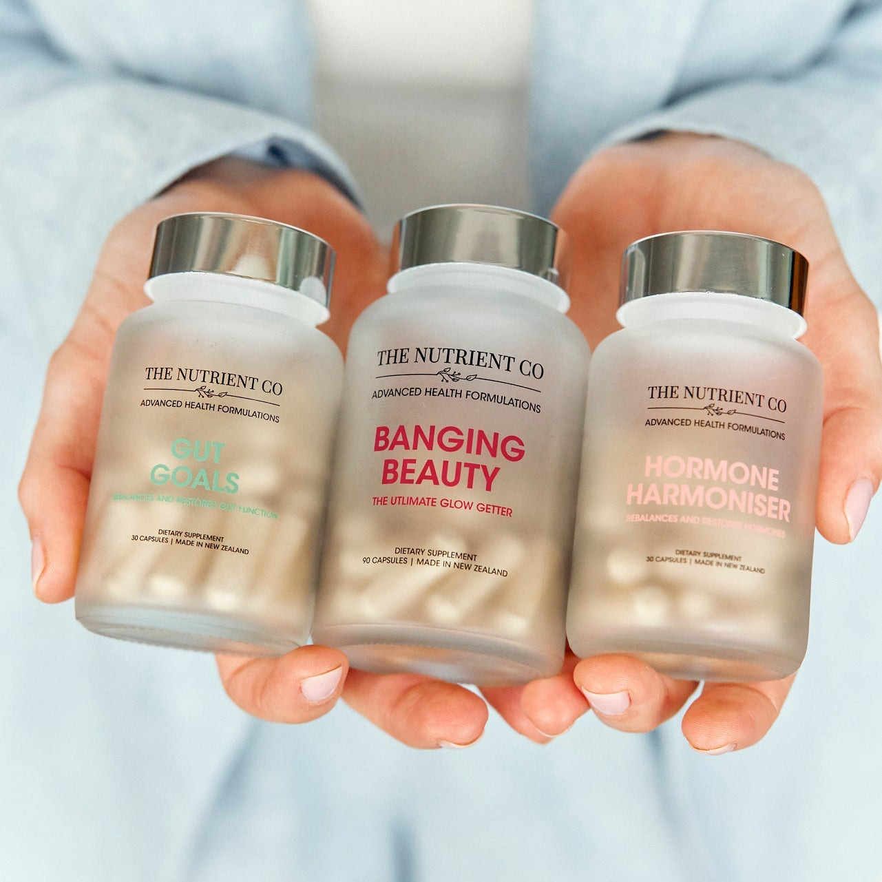 Three supplement bottles from The Nutrient Co held by a person against a light background