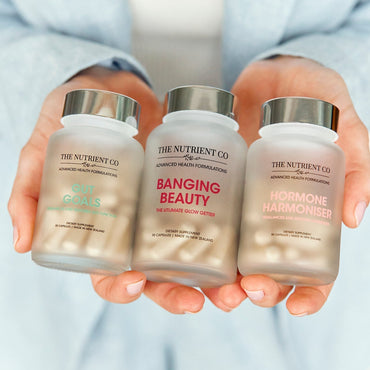 Three supplement bottles from The Nutrient Co held by a person against a light background